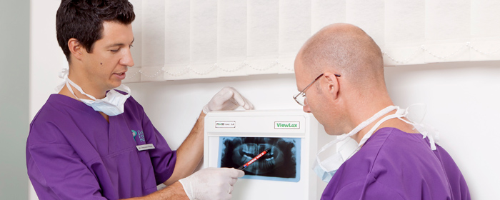 Dental care Hungary: cosmetic dentist is talking to patient, holding an X-ray in his hand.